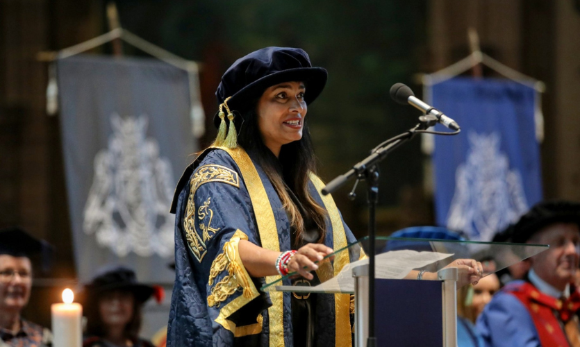 Chancellor Nisha Katona dressed in blue and gold robes behind a lectern giving a speech 